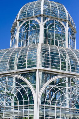 Küresel parlak bir ampulün yakın çekimi, parlak lifini karanlık bir arkaplanda sergiliyor. Şeffaf cam, karmaşık bobin dizaynını ortaya çıkararak sıcak ve çevresel bir ışık yayıyor. Ampul kısmen bir armatürle bağlantılı.