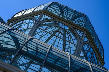 Küresel parlak bir ampulün yakın çekimi, parlak lifini karanlık bir arkaplanda sergiliyor. Şeffaf cam, karmaşık bobin dizaynını ortaya çıkararak sıcak ve çevresel bir ışık yayıyor. Ampul kısmen bir armatürle bağlantılı.