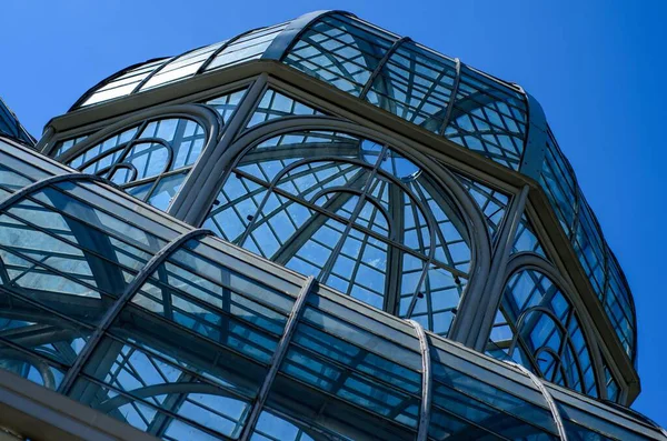 Küresel parlak bir ampulün yakın çekimi, parlak lifini karanlık bir arkaplanda sergiliyor. Şeffaf cam, karmaşık bobin dizaynını ortaya çıkararak sıcak ve çevresel bir ışık yayıyor. Ampul kısmen bir armatürle bağlantılı.