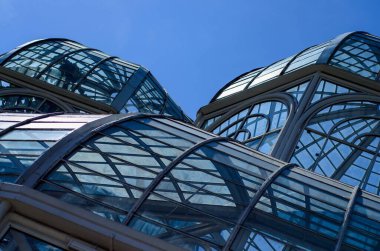 Küresel parlak bir ampulün yakın çekimi, parlak lifini karanlık bir arkaplanda sergiliyor. Şeffaf cam, karmaşık bobin dizaynını ortaya çıkararak sıcak ve çevresel bir ışık yayıyor. Ampul kısmen bir armatürle bağlantılı.