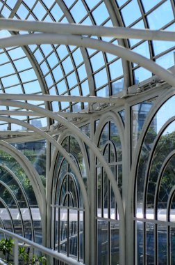 Küresel parlak bir ampulün yakın çekimi, parlak lifini karanlık bir arkaplanda sergiliyor. Şeffaf cam, karmaşık bobin dizaynını ortaya çıkararak sıcak ve çevresel bir ışık yayıyor. Ampul kısmen bir armatürle bağlantılı.