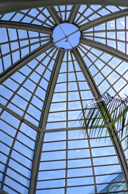 Küresel parlak bir ampulün yakın çekimi, parlak lifini karanlık bir arkaplanda sergiliyor. Şeffaf cam, karmaşık bobin dizaynını ortaya çıkararak sıcak ve çevresel bir ışık yayıyor. Ampul kısmen bir armatürle bağlantılı.