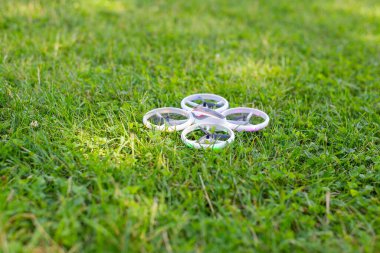 Taze yeşil çimlerin üzerinde LED ışıkları olan küçük beyaz bir kuadkopter drone 'un yakın çekimi. Modern oyuncak ya da insansız hava aracı açık havada uçmak ve eğlenmek için kullanılır..