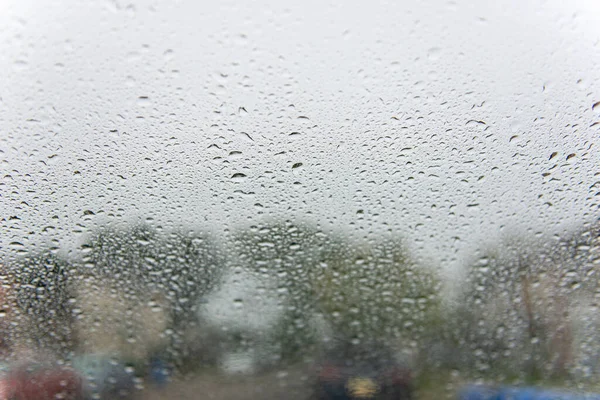 Bulanık bir sokak arka planına sahip bir araba camındaki yağmur damlalarının yakın görüntüsü. Hava temaları, arkaplanlar ve tasarım projeleri için soyut yağmurlu gün dokusu ideal.