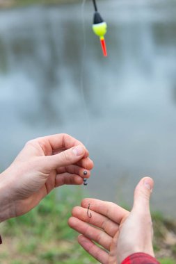 Balıkçı oltasını, batanları ve su kenarındaki şamandırayı ayarlayan ellerin yakın çekimi. Balıkçılık ve balıkçılık hazırlıklarının ayrıntılı görünümü.
