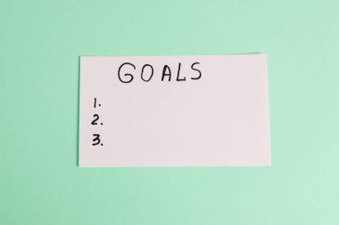 Asgari hedefler listesi konsepti beyaz kağıtta el yazısıyla yazılan hedefler ile pastel yeşil arka plan üzerinde. Planlama, motivasyon ve kişisel gelişim.