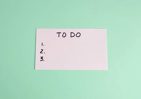 Pastel yeşil arkaplan üzerinde beyaz kağıt üzerine el yazısıyla yazılmış en az yapılacaklar listesi. Planlama, üretkenlik ve görev yönetimi kavramı.