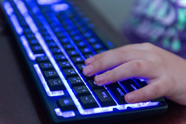 Karanlık bir ortamda mavi ışıklı oyun klavyesini kullanarak ellerinizi yakın plan çekin. Oyun, esportlar, teknoloji, bilgisayar oyunları ve dijital eğlence kavramı.