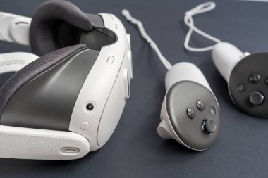 Karanlık yüzeyde modern VR kulaklıklar ve kontrolörlerin yakın çekimi. Sanal gerçeklik oyunu, metaevren, kopyalama alanı ile ilgili büyüleyici teknoloji ve eğlence kavramı.