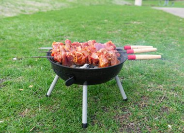 Çiğ et, yeşil çimlerin üzerinde mangal ızgarasında pişiyor. Barbekü partisi konsepti, piknik yemeği hazırlama.