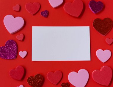 Kırmızı arka planda pembe, kırmızı ve parıltılı kalplerle çevrili boş beyaz kart modeli. Sevgililer Günü düz şablonu metin için kopyalama alanı ile yatıyordu.