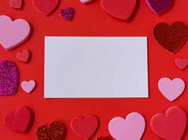 Kırmızı arka planda pembe, kırmızı ve parıltılı kalplerle çevrili boş beyaz kart modeli. Sevgililer Günü düz şablonu metin için kopyalama alanı ile yatıyordu.