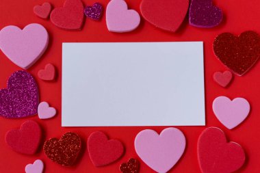 Kırmızı arka planda pembe, kırmızı ve parıltılı kalplerle çevrili boş beyaz kart modeli. Sevgililer Günü düz şablonu metin için kopyalama alanı ile yatıyordu.