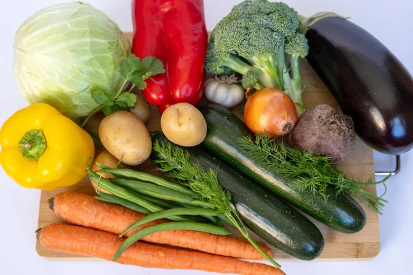 Lahana, dolmalık biber, brokoli, patlıcan, kabak, havuç, patates, soğan, sarımsak ve bambu tahtasındaki taze otlar da dahil olmak üzere çeşitli organik sebzeler. Beyaz arka plandaki bu renkli daire vegan tarifleri için mükemmel.