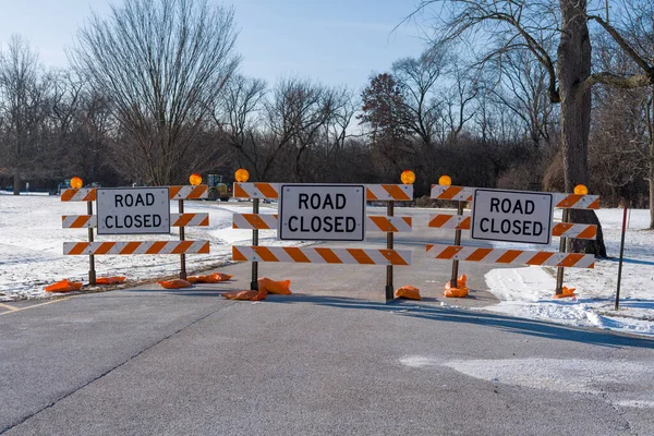 Turuncu ve beyaz çizgili bariyerlerin asfalt yolu kapattığı üç 