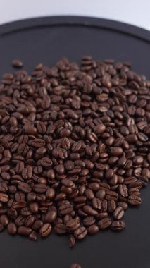 Siyah arka planda kavrulmuş kahve çekirdeklerinin 4K dikey sinema rotasyonu. 9: 16 portre görüntüsü, ağır çekim, zengin doku, karamsar minimalist tarz. Cep telefonu reklamları, Instagram makaraları ve TikTok için ideal.