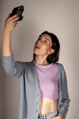 Süveter ve top giymiş genç bir kız arka planda klasik bir kamerayla poz veriyor..