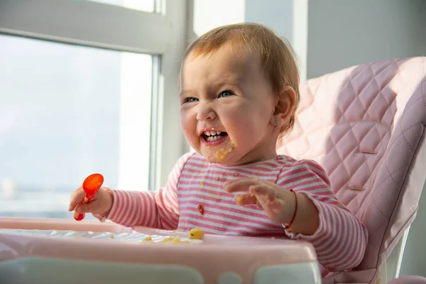 Little cute girl in a pink blouse eats at a pink table and laughing.