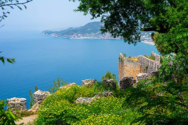Yukarıdan Alanya şehrinin güzel manzarası. Yeşil ağaçlara gömülü kadim bir savunma duvarı ve bir tarafında mavi deniz, diğer tarafında dağlar olan bir tatil köyü..