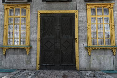 Eski bir evin pencere ve kapıları. Pencereleri, kapıları ve gri bir duvarı olan sarı ahşap platformlar. Çubuklu pencereler.