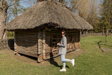 Güzel, şık giyimli bir kız eski bir kır evinin arka planında sazdan bir çatı altında..