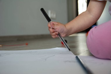 Küçük tatlı kız yere beyaz kağıt çizer.