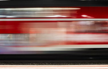 Kırmızı bir yolcu treni, hareket bulanıklığı yaratan uzun bir pozla fotoğraflanır. Raylar boyunca giden tren uzun süre maruz kaldığı için bulanık..