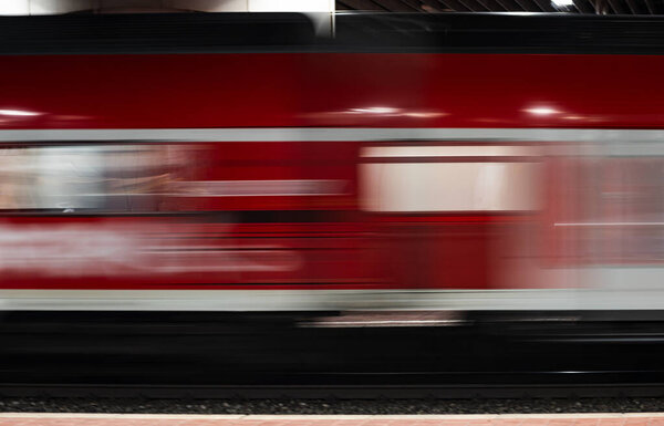 A red passenger train is photographed with a long exposure, creating a motion blur effect. The train traveling along the tracks is blurred due to the long exposure.