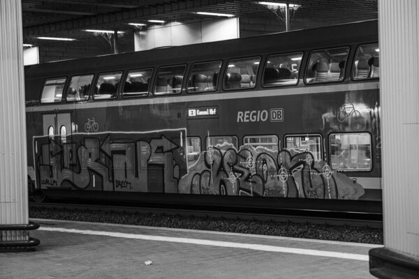 Kassel, Germany - 01.11.2025: A double-decker passenger train at a deserted station at night. A car of a regional train in Germany covered in graffiti. Black and white image.