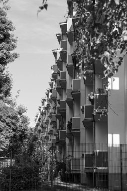 Kırmızı balkonları ve yanında köknar ağaçları olan çok katlı bir bina. Balkonları olan bir Alman apartmanı. Bazı balkonlarda çiçekler ve şemsiyeler vardır..