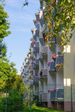Kırmızı balkonları ve yanında köknar ağaçları olan çok katlı bir bina. Balkonları olan bir Alman apartmanı. Bazı balkonlarda çiçekler ve şemsiyeler vardır..