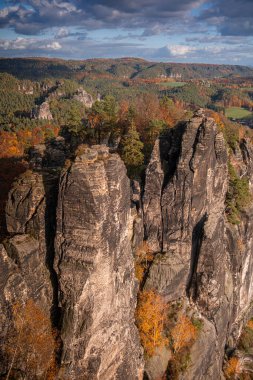 Sakson İsviçre, Bastei Doğa Koruma Alanı. Benzersiz kaya oluşumlarının görüntüsü. Sonbahar ormanının üzerinde taş sütunlar yükselir..