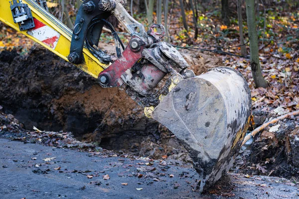 Çamurla kaplı küçük bir kazıcı kovası asfalt bir yolda duruyor. Parkta kazı çalışmasında bir mola.