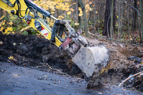 Çamurla kaplı küçük bir kazıcı kovası asfalt bir yolda duruyor. Parkta kazı çalışmasında bir mola.
