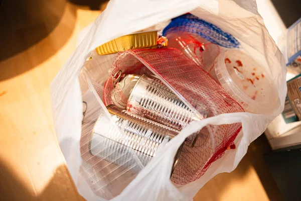 Geri dönüşüm için şeffaf bir plastik torba içinde sıralanmış ev atıkları yakın çekim. İçinde alüminyum kutular ve plastik kaplar var. Evdeki çevre bilinci, sürdürülebilirliği ve sorumlu çöp yönetimini vurguluyor.