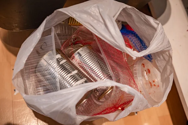 Geri dönüşüm için şeffaf bir plastik torba içinde sıralanmış ev atıkları yakın çekim. İçinde alüminyum kutular ve plastik kaplar var. Evdeki çevre bilinci, sürdürülebilirliği ve sorumlu çöp yönetimini vurguluyor.