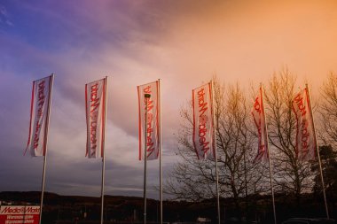 Almanya, Eisenach 10.11.2026: Dramatik bir gökyüzüne karşı ikonik kırmızı MediaMarkt logosunu gösteren çoklu dikey bayraklar.