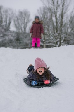 Karlı bir tepeden kayan küçük bir kız parlak bir kar kaydırağıyla. Soğuk bir günde, bir orman parkında aktif kış oyunlarının keyfini çıkaran mutlu bir çocuk..