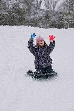 Karlı bir tepeden kayan küçük bir kız parlak bir kar kaydırağıyla. Soğuk bir günde, bir orman parkında aktif kış oyunlarının keyfini çıkaran mutlu bir çocuk..