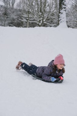 Karlı bir tepeden kayan küçük bir kız parlak bir kar kaydırağıyla. Soğuk bir günde, bir orman parkında aktif kış oyunlarının keyfini çıkaran mutlu bir çocuk..