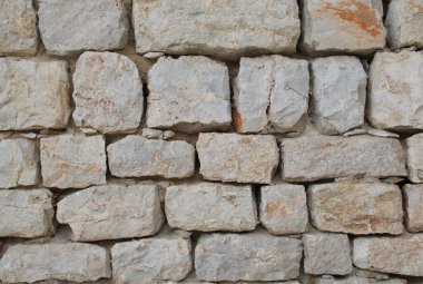 Üst üste dizilmiş taş duvarın yüksek çözünürlüklü yakın çekimi kaba, doğal dokuları, düzensiz şekilleri ve arka plan, mimari tasarım, inşaat malzemeleri ve doku için toprak rengi ideallerini gösterir.