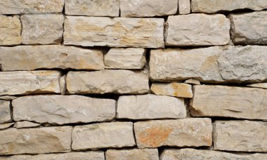 Üst üste dizilmiş taş duvarın yüksek çözünürlüklü yakın çekimi kaba, doğal dokuları, düzensiz şekilleri ve arka plan, mimari tasarım, inşaat malzemeleri ve doku için toprak rengi ideallerini gösterir.