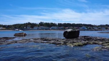 St. Lawrence Nehri, Saint-Ulric-de-Matane, Quebec, Kanada, 2025 'te kilise çan kulesiyle pitoresk bir sahil köyünün kıyısındaki sudan iki kaya yükselir..