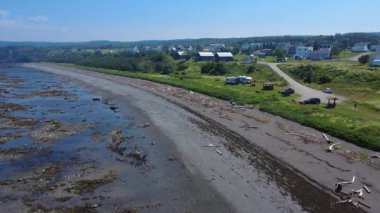 Küçük bir sahil köyünün kenarına sürüklenen dallarla dolu bir plaj yakınında birkaç turistin bulunduğu küçük bir halk parkının havadan görüntüsü. Sainte-Felicit, Quebec, Kanada, 2025.