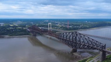 İki dönemin buluştuğu yer. Pierre-Laporte Köprüsü ve Quebec Köprüsü muhteşem St. Lawrence Nehri 'ne tepeden bakan bulutlu bir gökyüzünün altında panoramik bir manzara. Kanada, 2025.