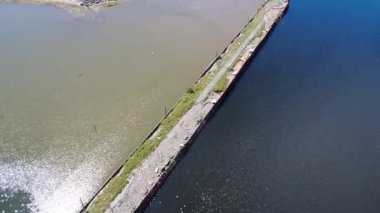 Eski terk edilmiş bir rıhtımın havadan görünüşü farklı renklerde iki su kütlesini ayırıyor, mavi ve kahverengi, dalgaların üzerinde güneşin yansıması. Campbellton, NB, Kanada, 2025.