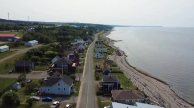 Baie-des-Sables köyünün kıyı yolu ve St. Lawrence nehrinin kıyısındaki kumlu plajının havadan görünüşü, ufukta rüzgarlı türbinler görülüyor. Quebec, Kanada. 2025.