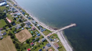 Kumlu bir sahil boyunca uzanan bir sahil köyünün panoramik hava manzarası. Eski bir taş rıhtım St. Lawrence Nehri 'nin sakin mavi sularına doğru uzanırken evler dar sokaklar boyunca uzanır. Baie-des-Sables, Quebec, Kanada, 2025.