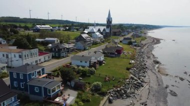 Rue de la Mer 'in Baie-des-Sables köyündeki kiliseye giden hava manzarası. Etrafı rüzgâr türbinleri ve St. Lawrence nehri ile çevrili renkli evlerle dolu. Gasp Yarımadası, Quebec, Kanada, 2025.