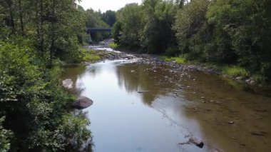 Huzurlu bir nehir orman boyunca kayalık bir yatağın üzerinden taşra yolundaki bir köprünün beton temeline akar. Tartigou Nehri, Baie-des-Sables, Quebec, Kanada.